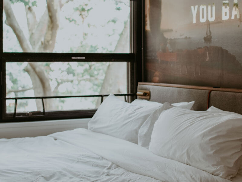 A made up bed with white bedding and window view of trees