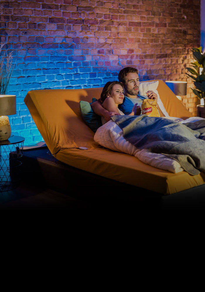 Couple lying in box spring bed with CosyLift angled and watching a movie