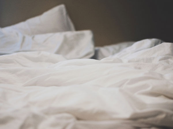 Nahaufnahme von einem ungemachten Bett mit weißer Bettwäsche