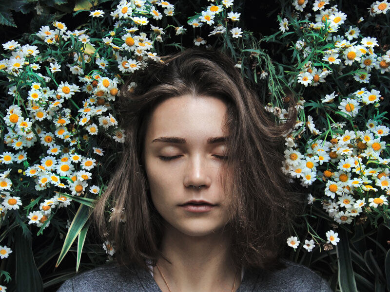 Portrait einer Frau mit geschlossenen Augen, die in einer Blumenwiese liegt