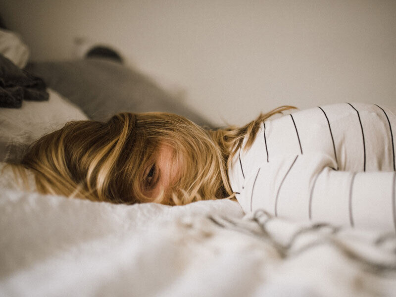 Frau liegt erschöpft im Bett mit Haaren im Gesicht